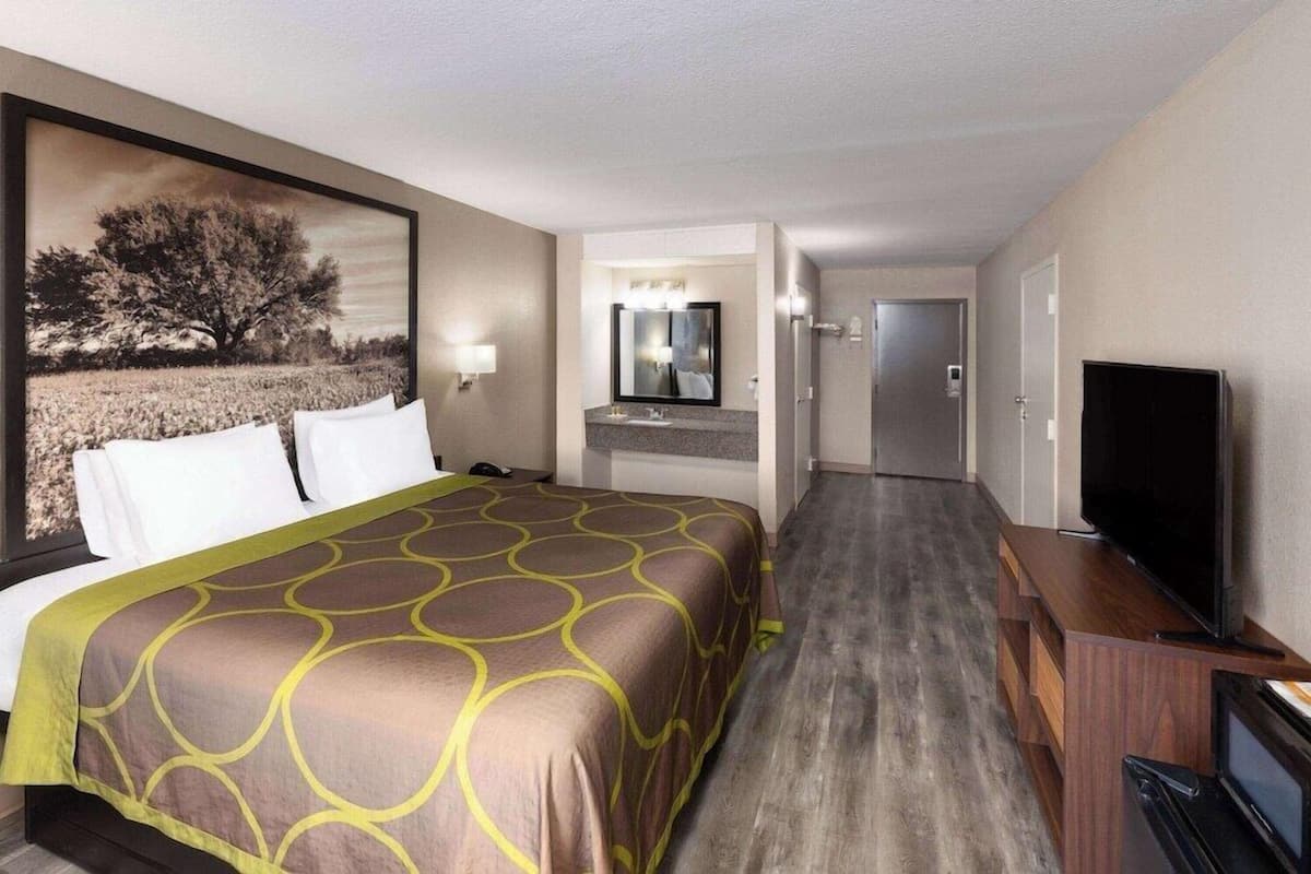 A hotel room with a bed, a television, a mirror, and a kitchenette.