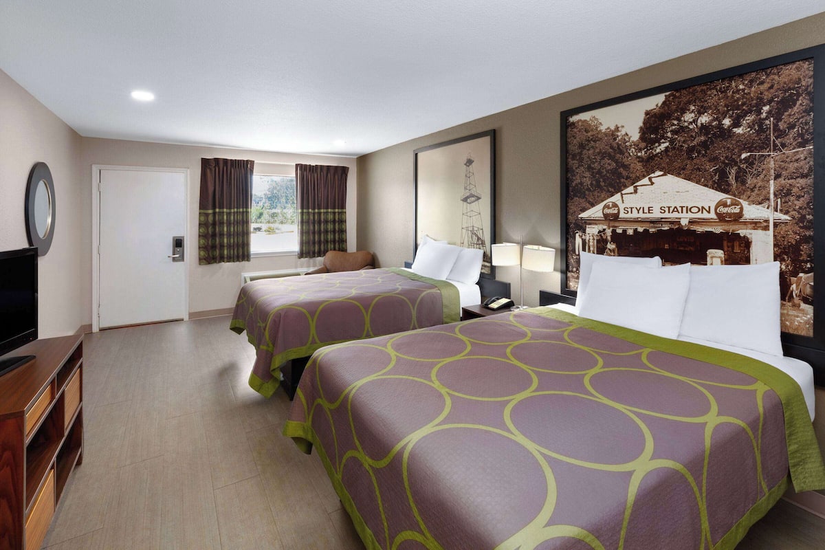A hotel room with two beds, a television, a desk, and a window with curtains.