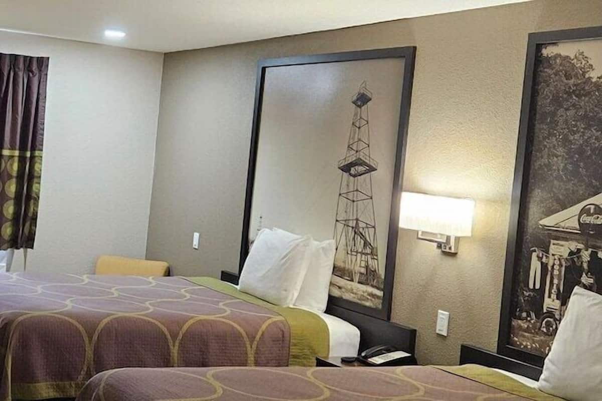 A hotel room with two beds, a desk with a computer, a window with curtains, and a wall-mounted artwork.