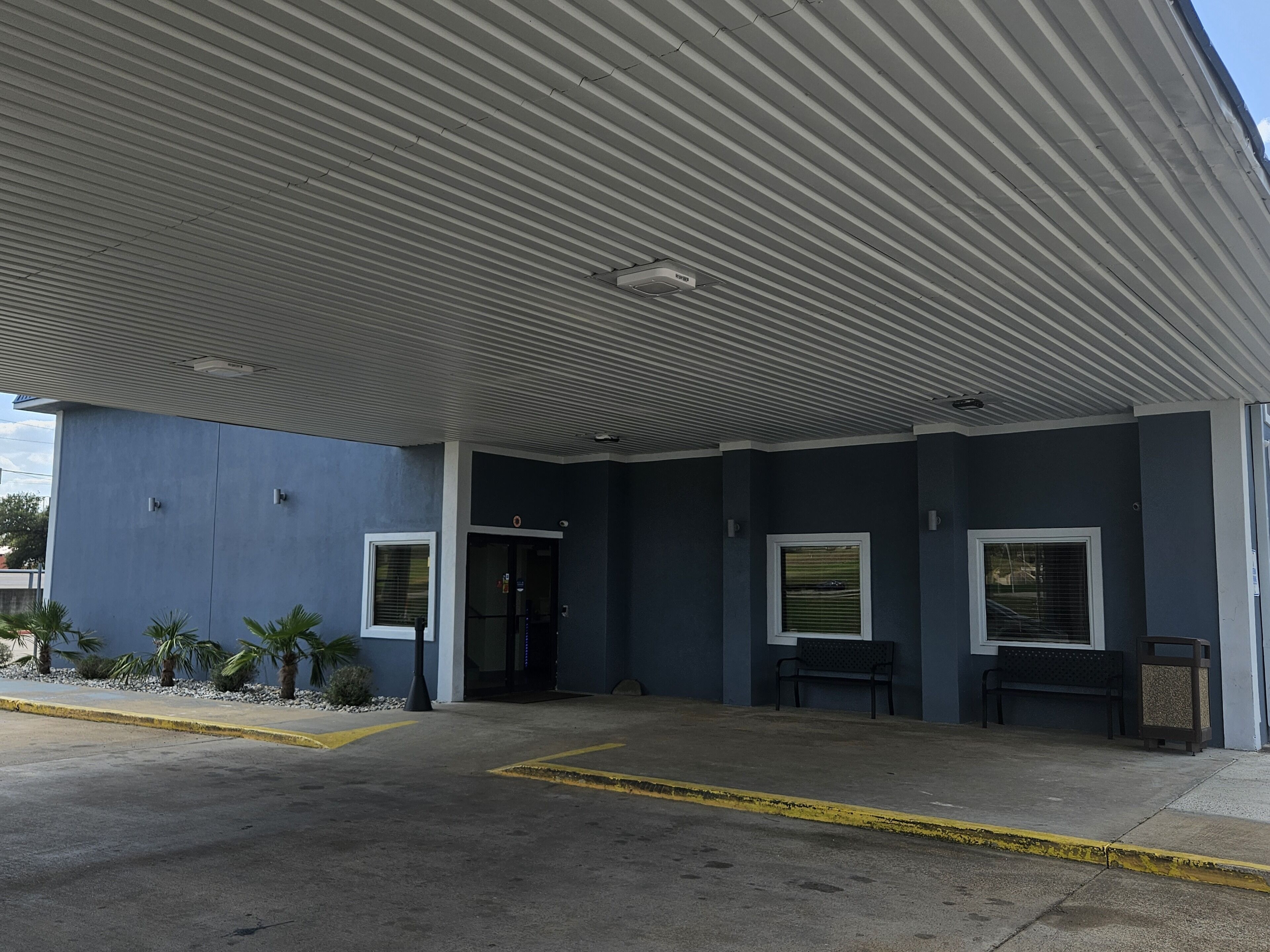A building with a flat roof, a covered entrance, and a paved area with yellow lines.