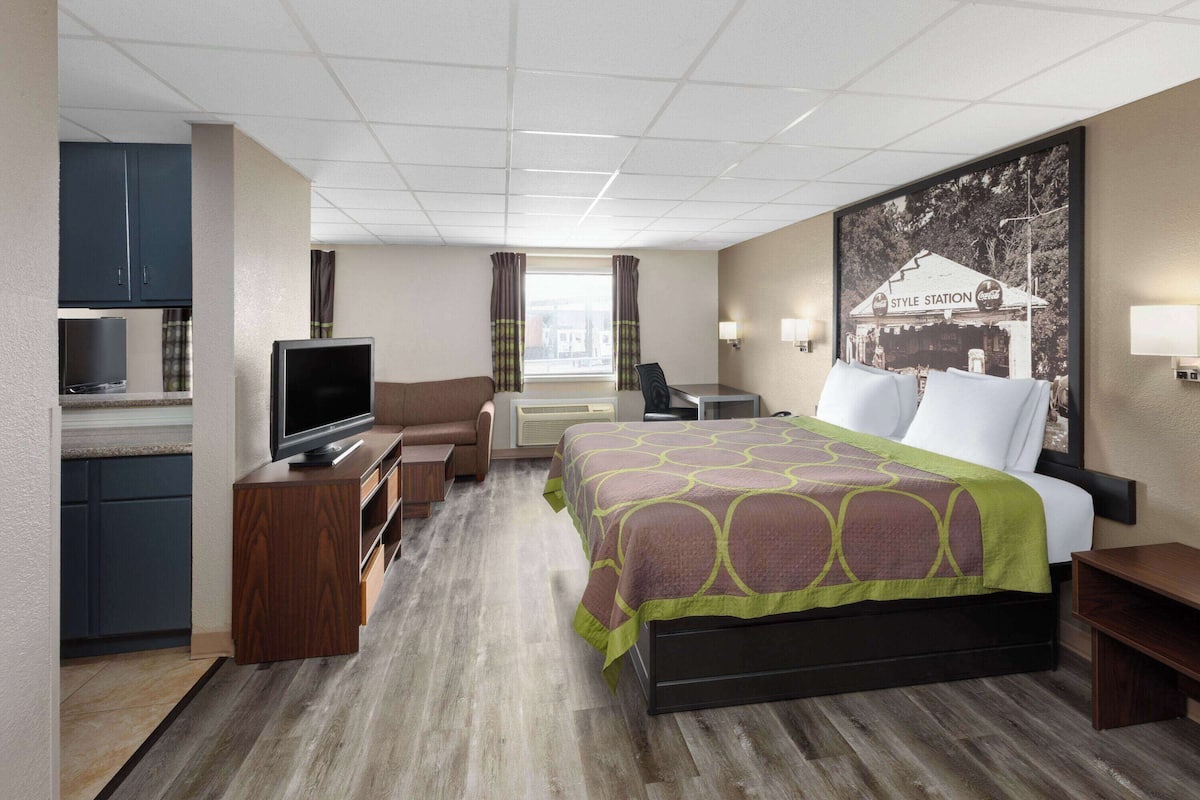 A hotel room with a bed, a TV, a desk, and a kitchenette.