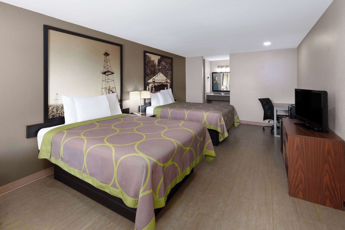 A hotel room with two beds, a desk, a television, and artwork on the walls.