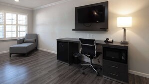 Un espacio de oficina moderno con un televisor de pantalla plana grande, un escritorio con una silla, un refrigerador pequeño y una lámpara.