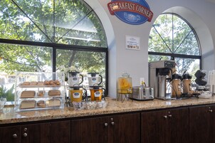Una barra de desayuno con una máquina de café, tostadora y una vitrina con pasteles.