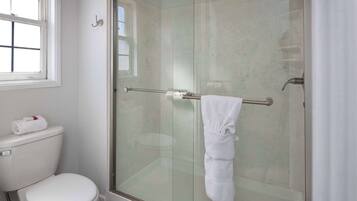 A bathroom with a glass-enclosed shower, a toilet, and a towel rack with a towel.
