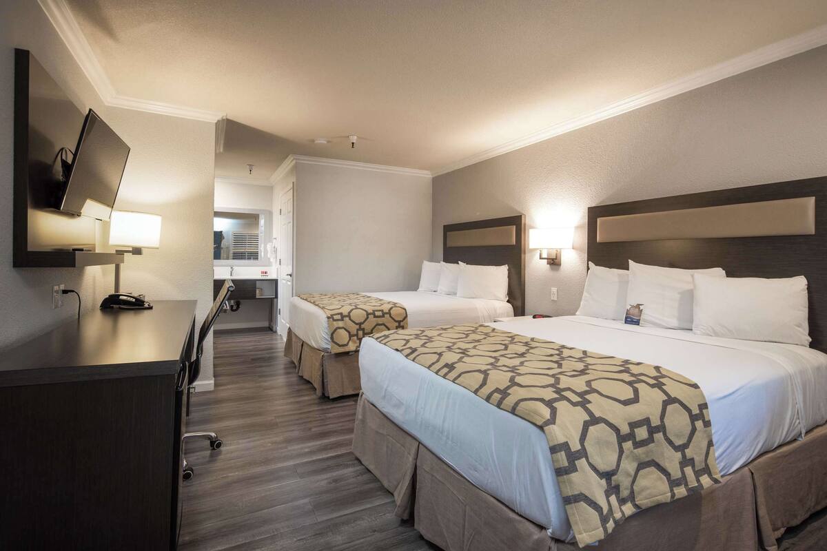 A hotel room with two beds, a desk, and a TV.
