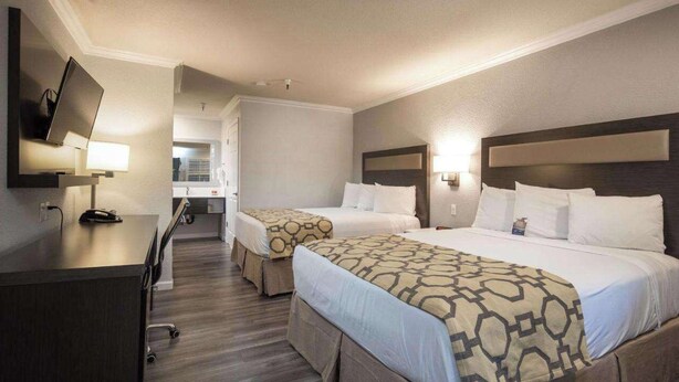Habitación de hotel con dos camas, un escritorio, televisión y baño a la vista.