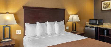 Una habitación de hotel con una cama grande, dos mesitas de noche con lámparas, un microondas y un refrigerador.