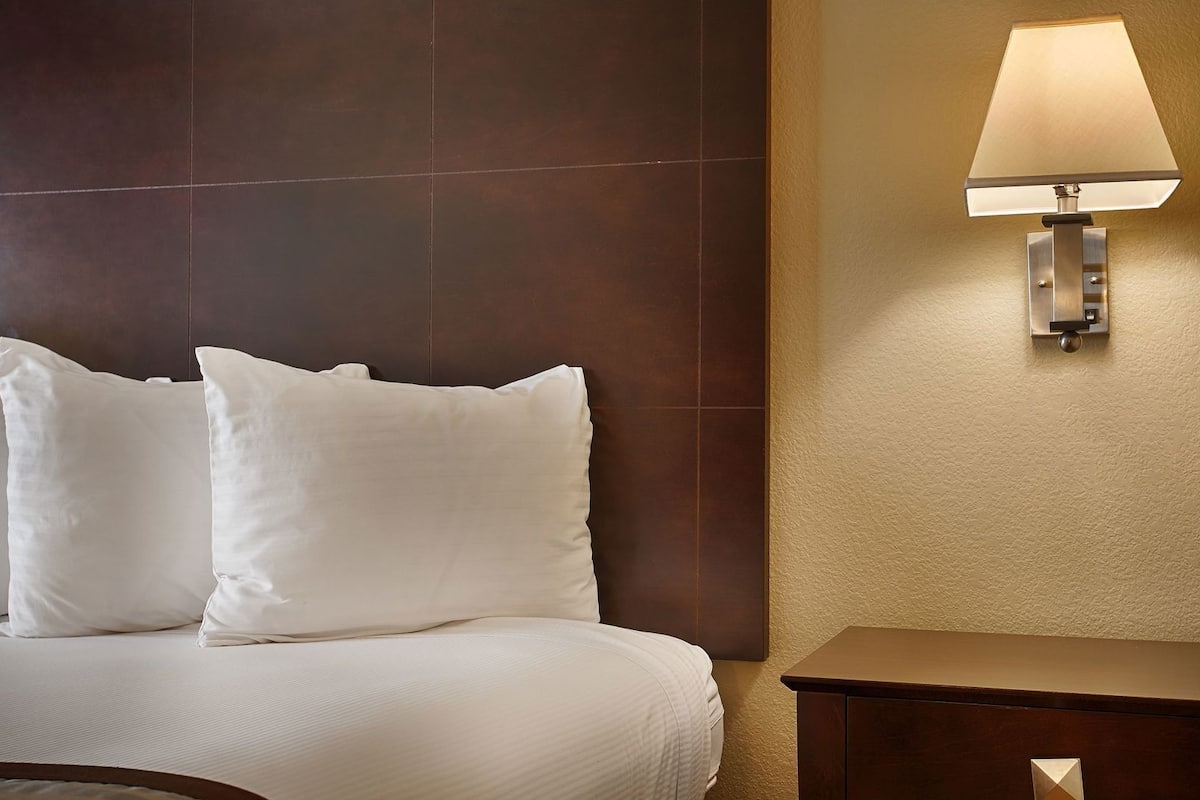 Een hotelkamer met een bed, twee kussens, een nachtkastje en een wandlamp.