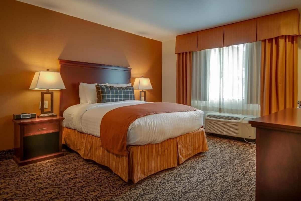 Een hotelkamer met een groot bed, twee bedlampen, een raam met gordijnen, een bureau en een vloerkleed.