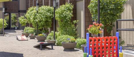 An outdoor area with potted plants, a red and blue play structure, and a building with a brick facade.