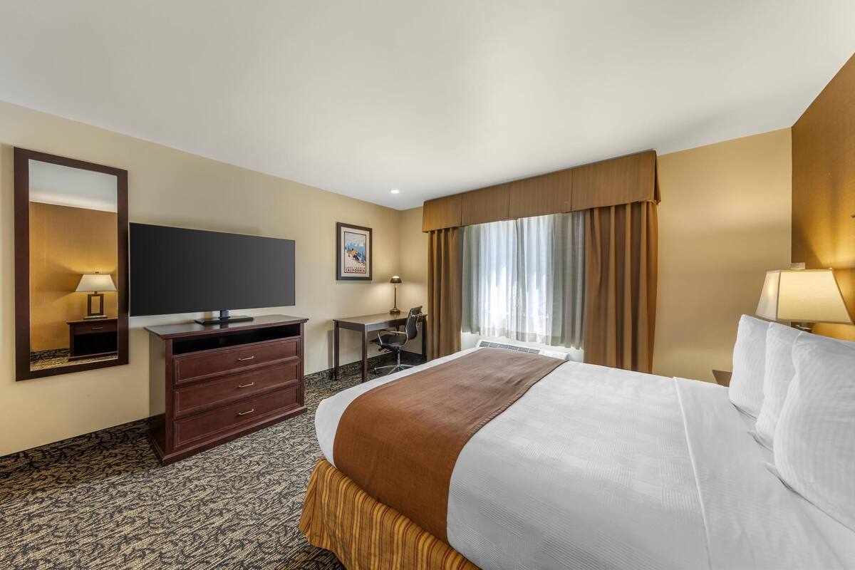 Een hotelkamer met een groot bed, een bureau, een stoel, een televisie, een spiegel en een raam met gordijnen.