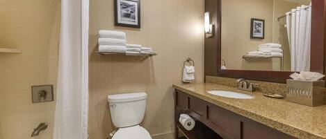 A bathroom with a toilet, sink, and shower. There are towels on a shelf and a mirror above the sink.