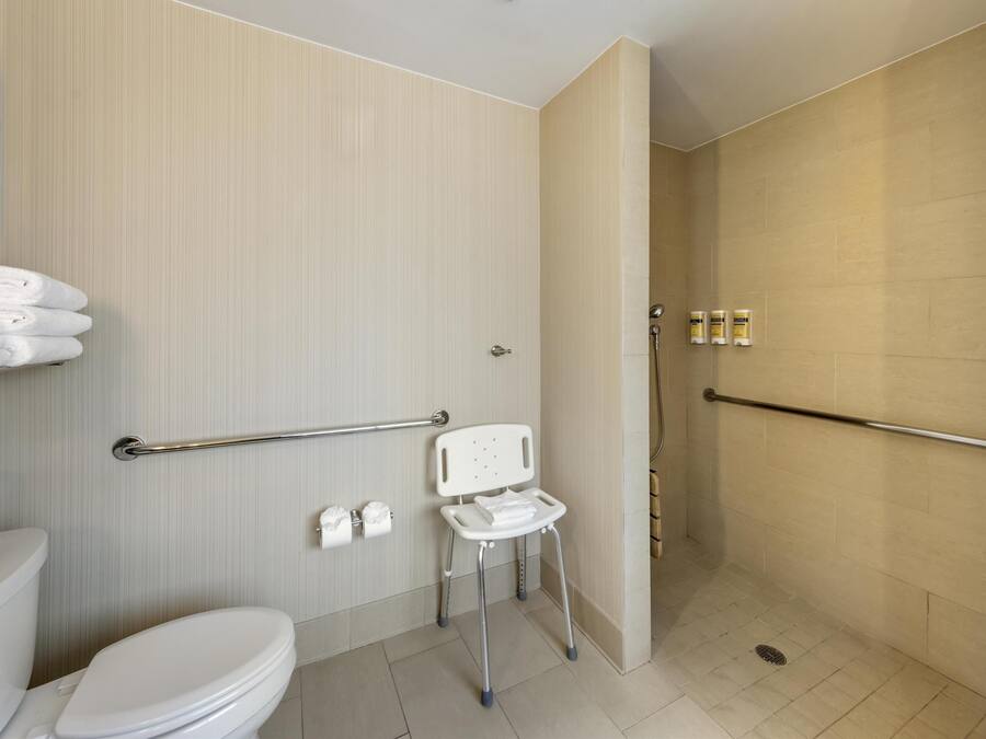 Une salle de bain moderne équipée de toilettes, d’une barre d’appui, d’un espace douche et d’un banc accessible aux personnes en fauteuil roulant.