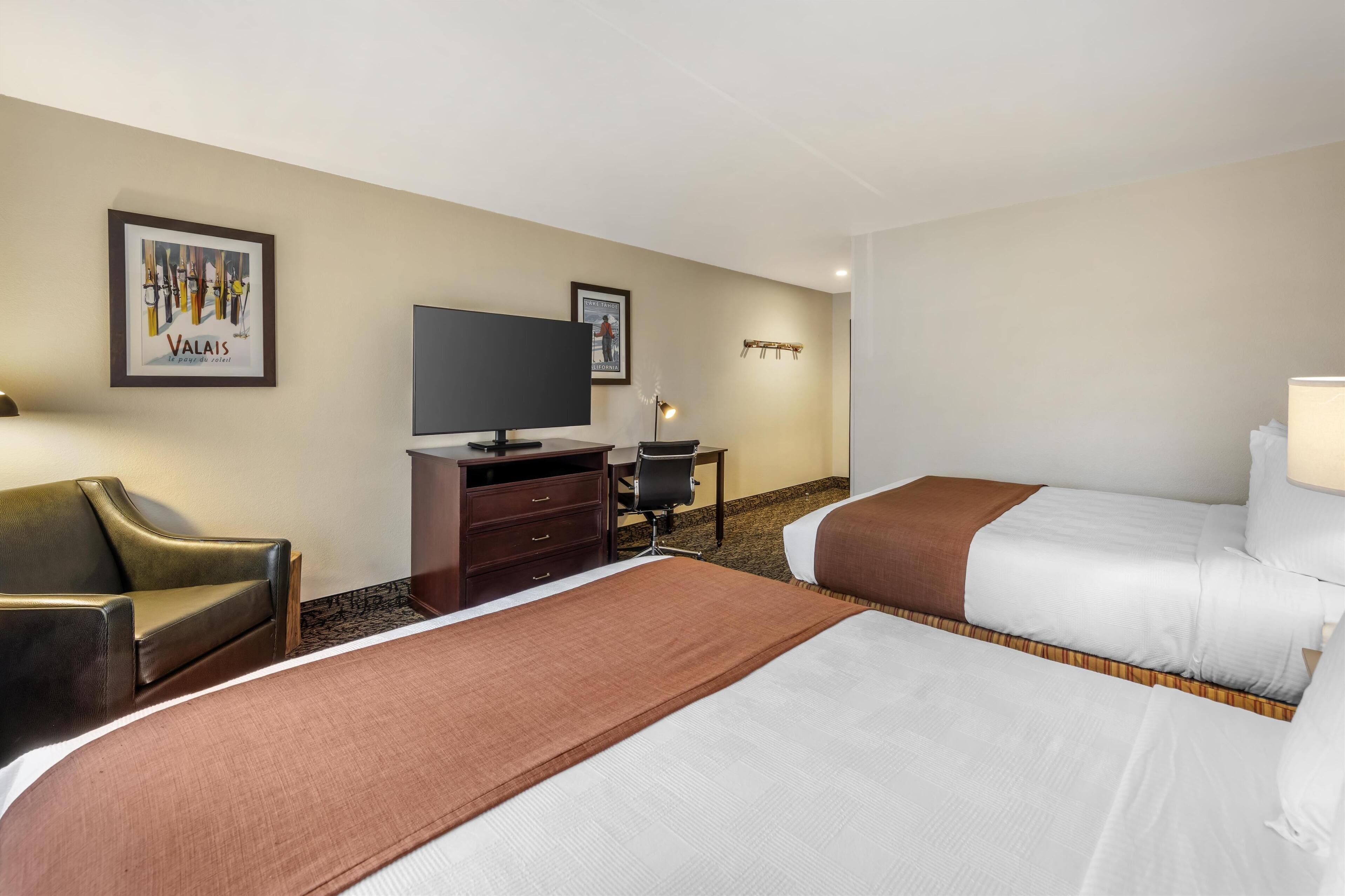 A hotel room with two beds, a TV, a desk, and a chair.