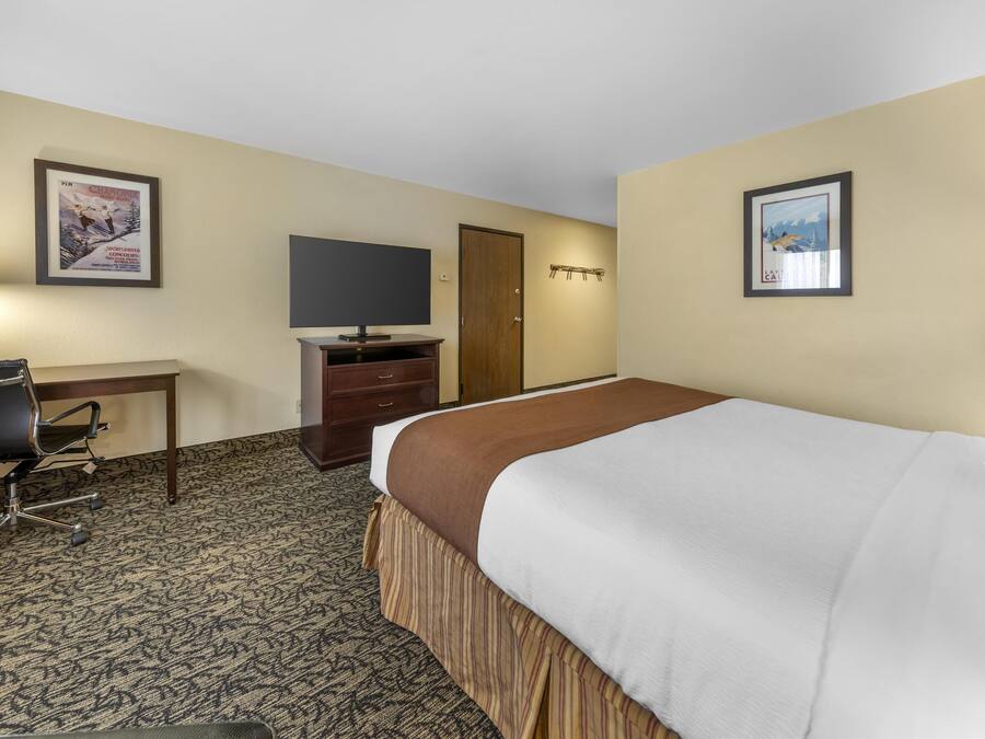 A hotel room with a bed, a desk with a chair, a television, and a wardrobe.