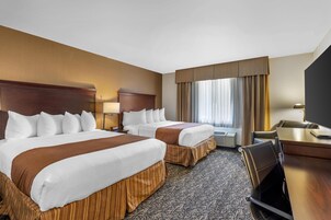 A hotel room with two beds, a desk, and a chair.