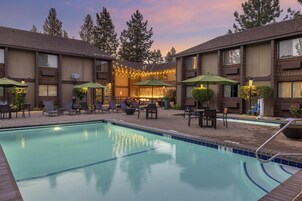 A pool area with lounge chairs and umbrellas, surrounded by buildings with a brick facade and large windows.
