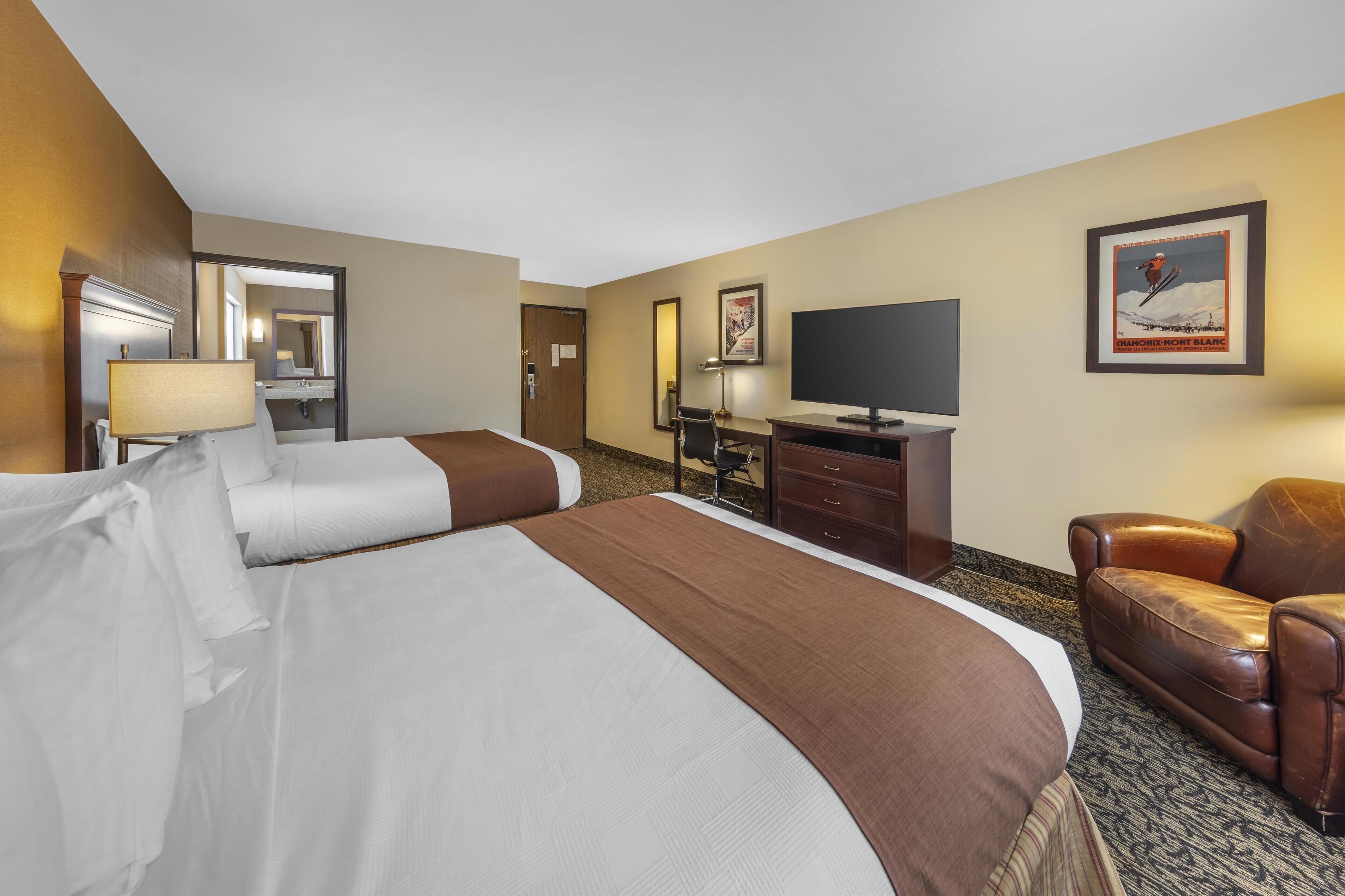 A hotel room with two beds, a desk, a chair, a television, and a framed picture on the wall.