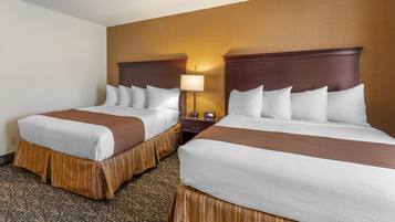A hotel room with two beds, each with a brown headboard, white bedding, and a patterned carpet.