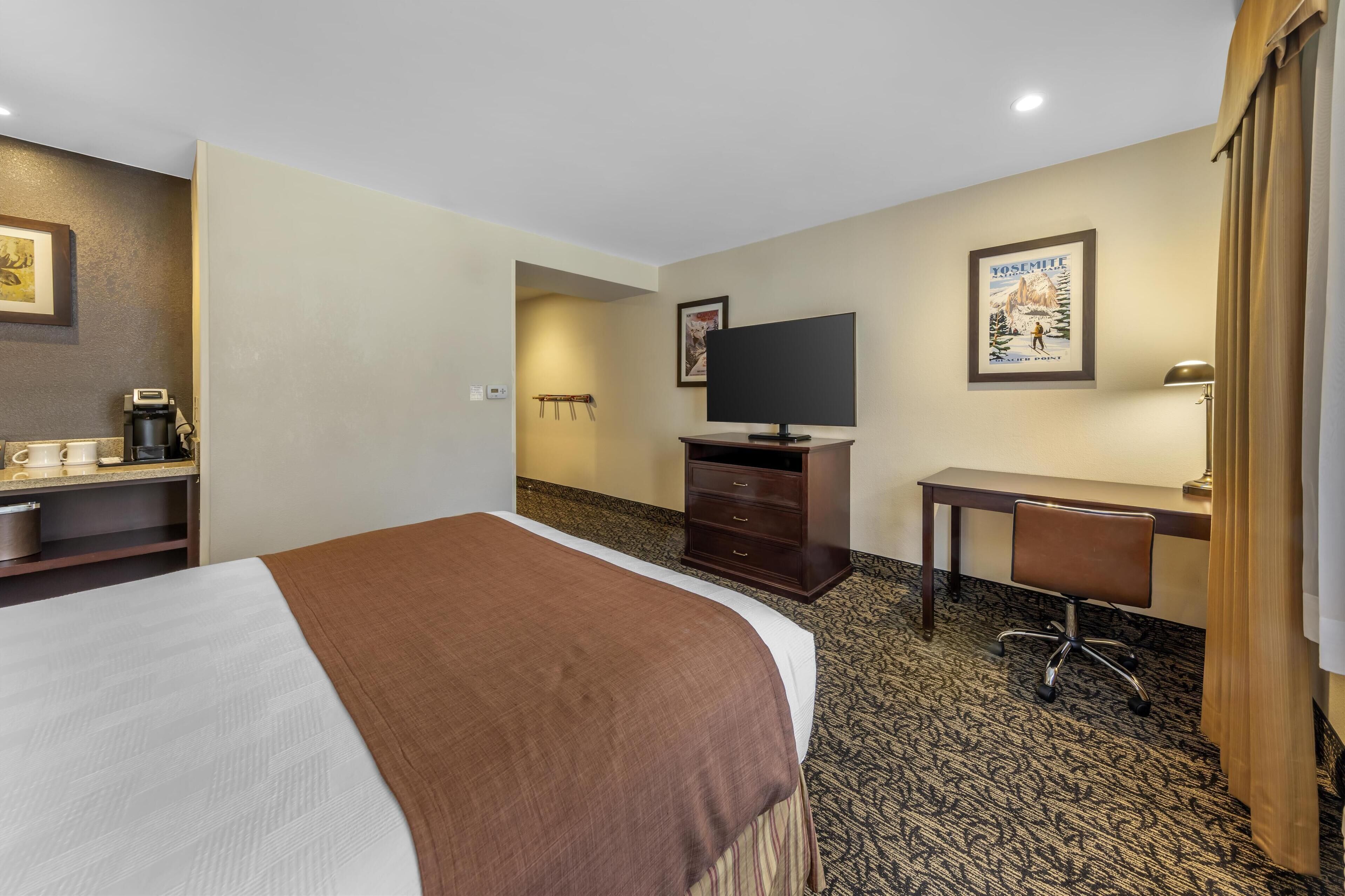 A hotel room with a bed, a desk, a chair, a television, and a poster on the wall.