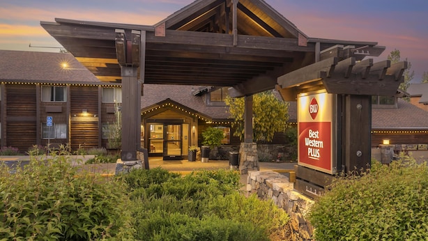 Entrada de un hotel con un porche cubierto, mobiliario exterior y un cartel que anuncia 'Best Western PLUS'.