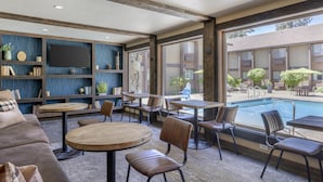 Un área de estar interior moderna con vistas a una piscina, que incluye un sofá, mesas redondas y sillas.