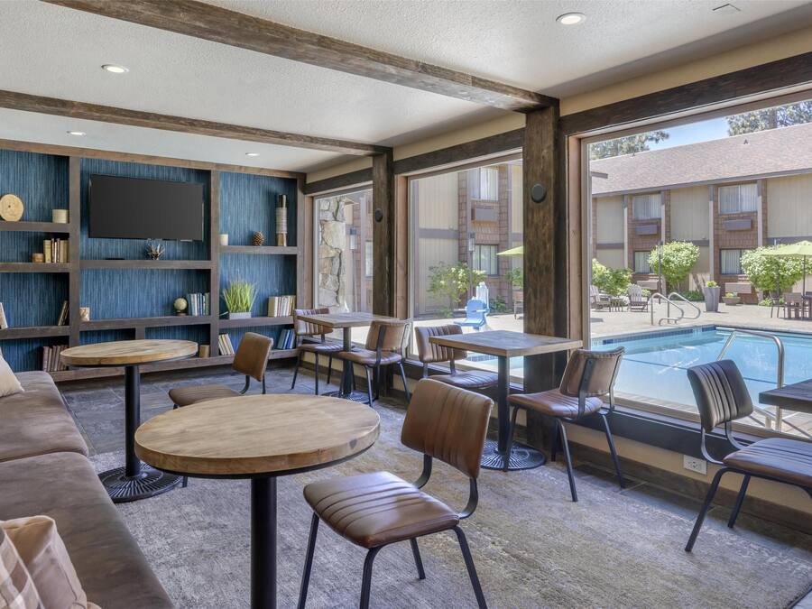 Un espace de détente intérieur moderne, avec vue sur la piscine, comprenant un canapé, des tables rondes et des chaises.
