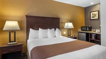 A hotel room with a large bed, two bedside tables with lamps, a microwave, a coffee maker, and a framed picture on the wall.