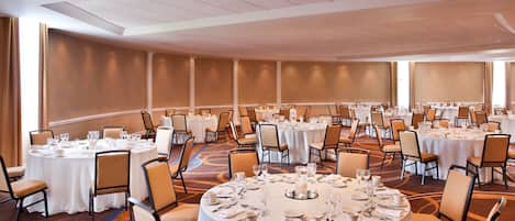 A large conference room with multiple round tables set for dining, equipped with chairs and table settings.