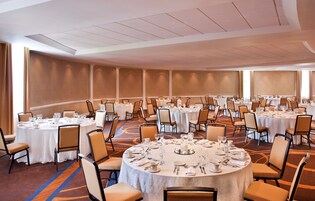 Un amplio salón de conferencias con varias mesas redondas dispuestas para comer, equipado con sillas y cubiertos.