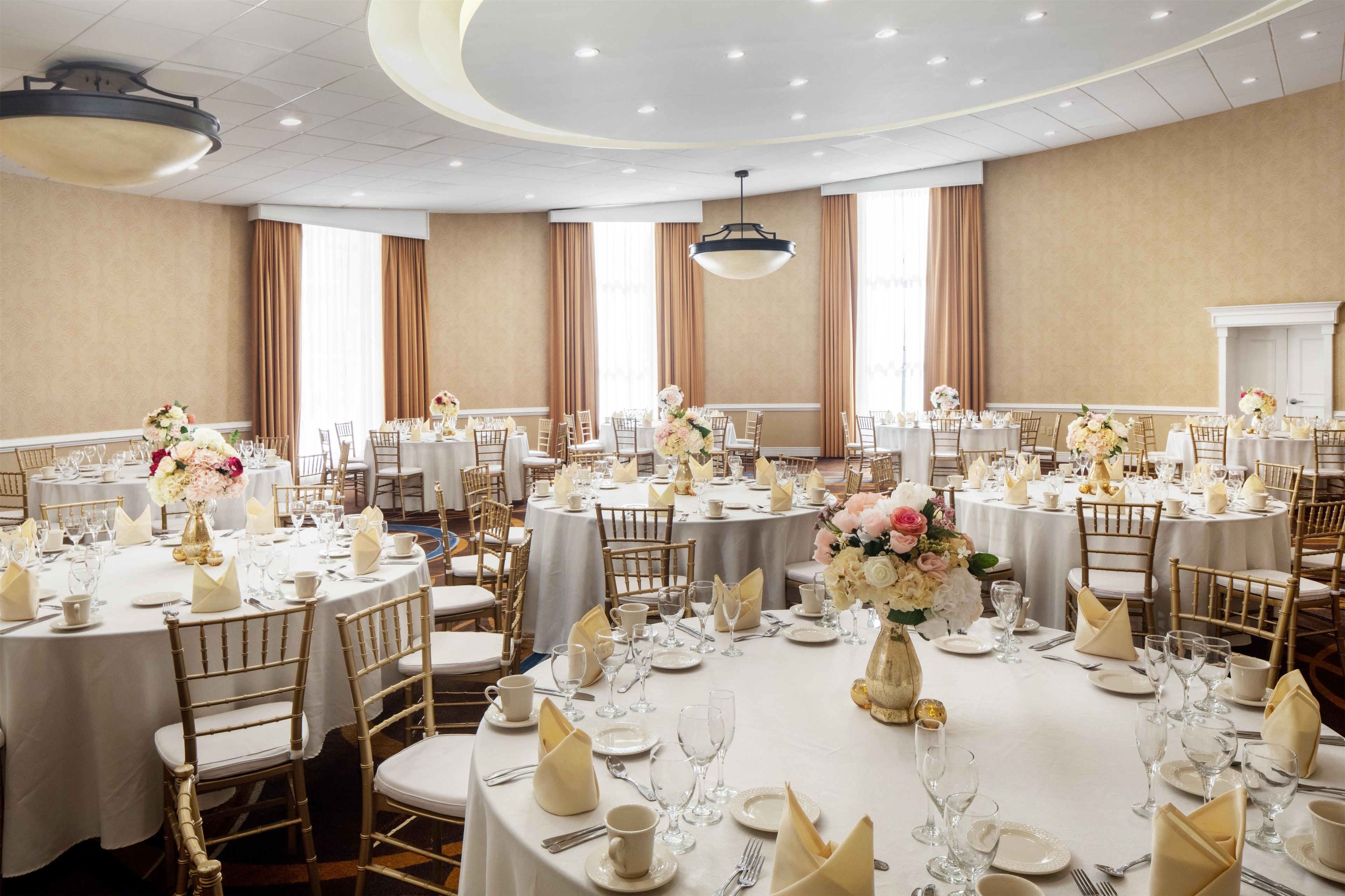 Un salón de banquetes con mesas redondas, manteles blancos y sillas doradas.