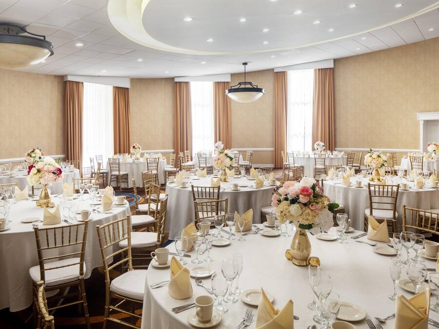 A banquet hall with round tables, white tablecloths, and gold chairs.