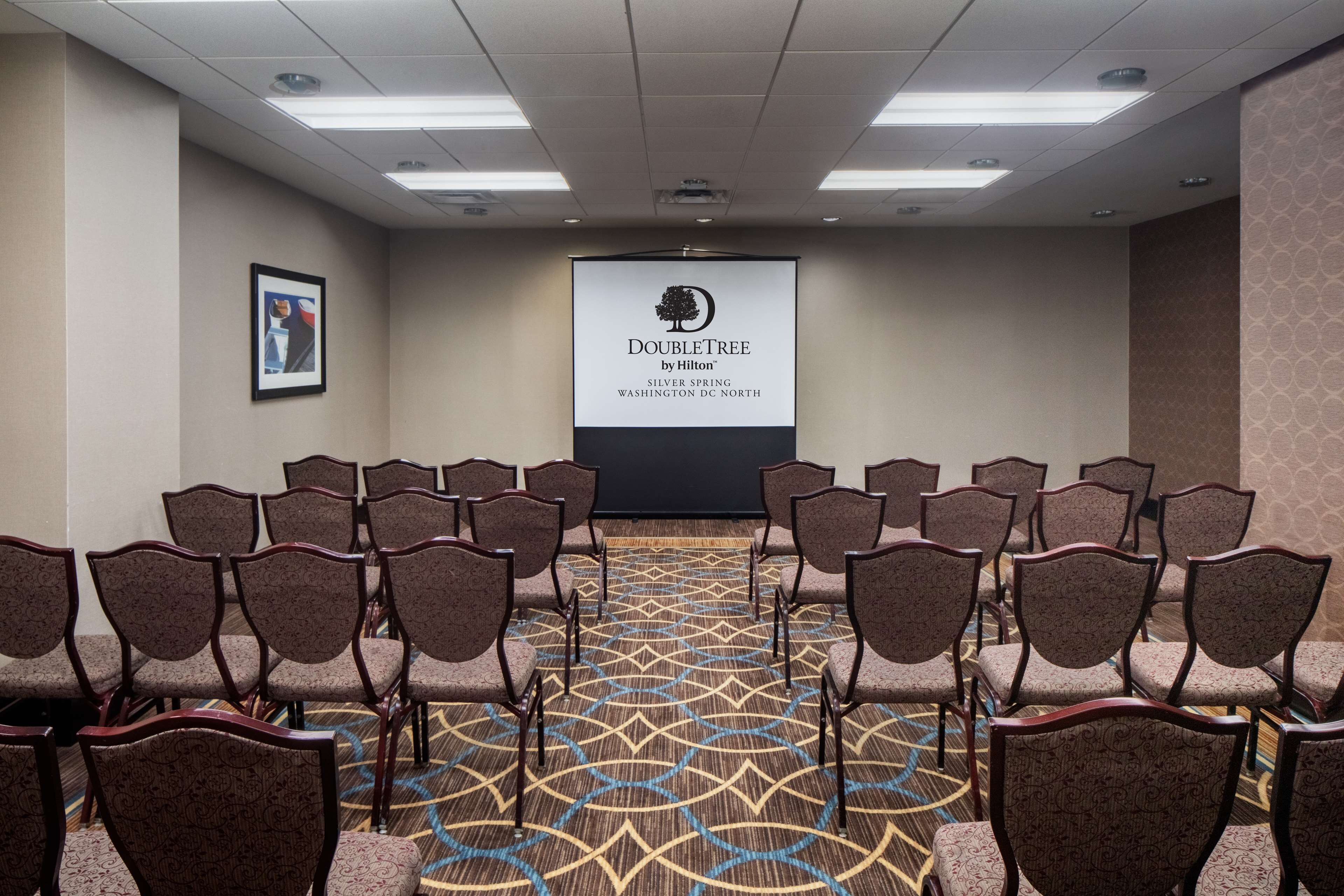 A conference room with rows of chairs facing a projection screen displaying "DOUBLETREE by Hilton" and "Silver Spring, Washington DC North".