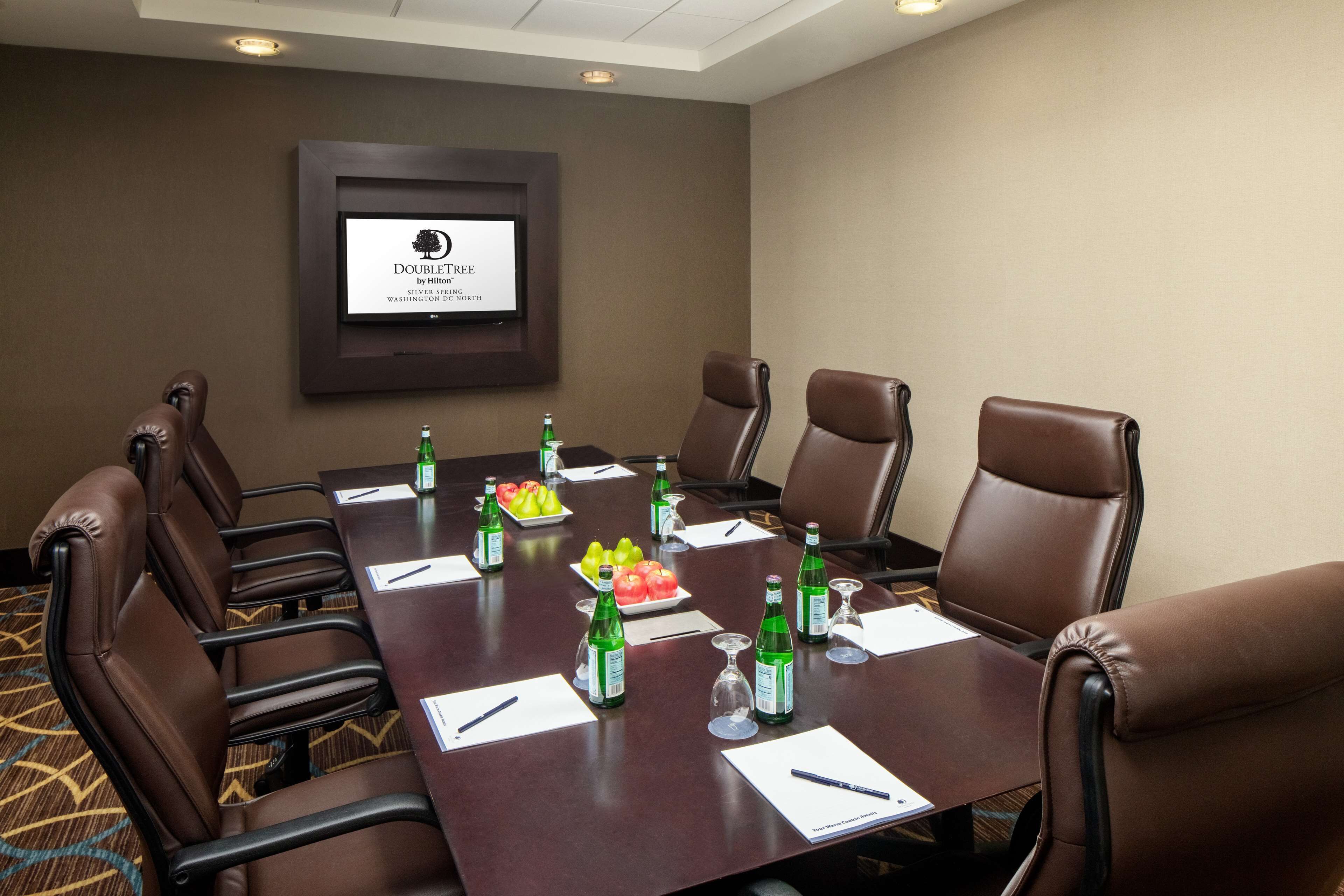 Ein Konferenzraum mit einem langen Tisch, braunen Ledersesseln und einem Bildschirm, der das DoubleTree-Logo zeigt.