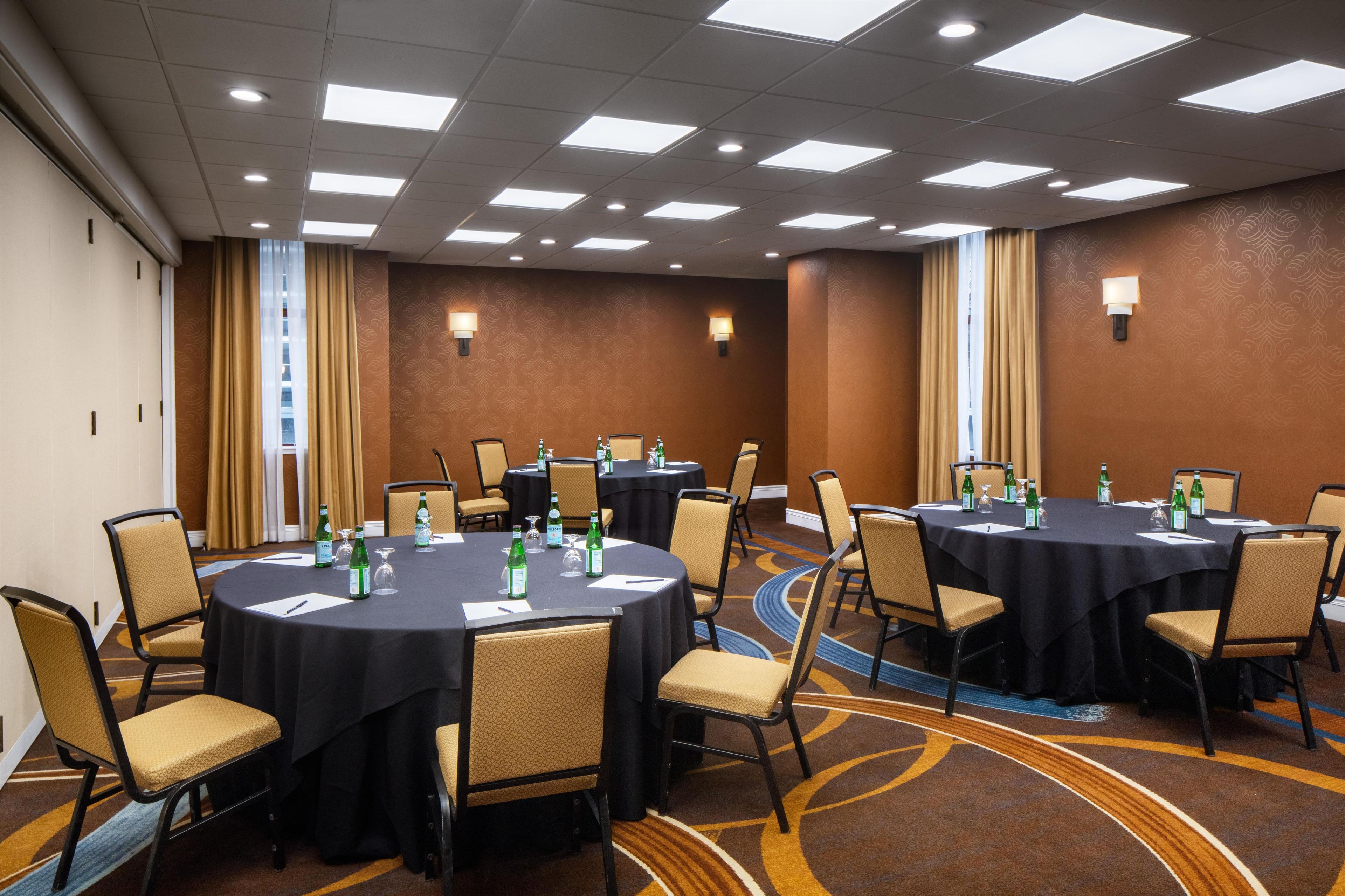 A conference room with round tables, chairs, and tables set with water bottles and glasses.