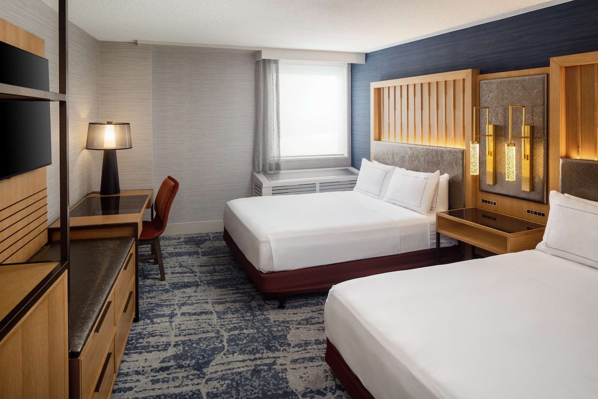 A hotel room with two beds, a desk, a TV, and a window with curtains.