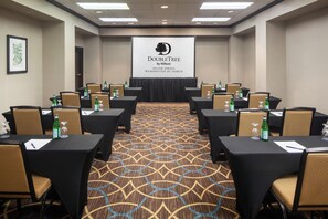 A conference room with tables, chairs, and a projector screen displaying the hotel's name and location.
