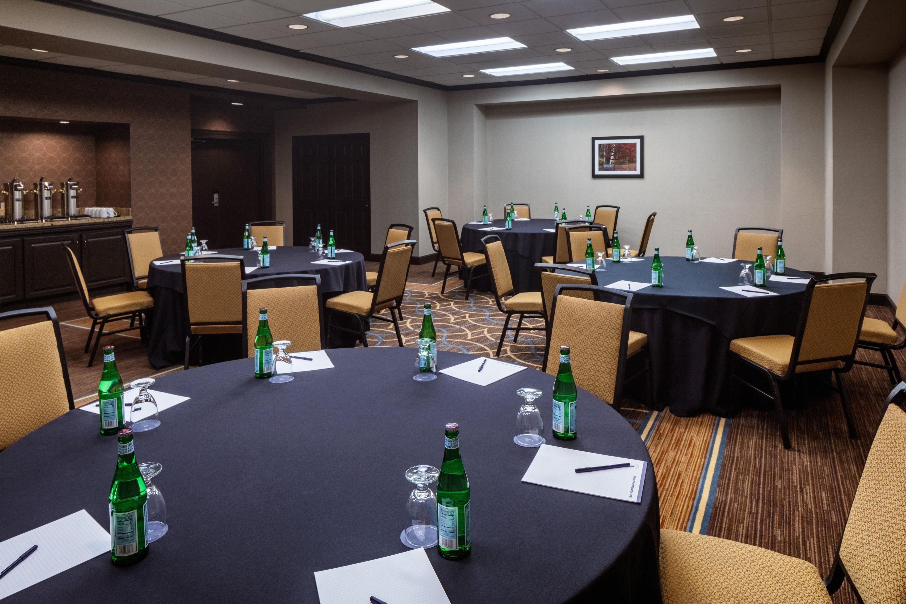 A conference room with round tables, chairs, and tables set with bottles and glasses.