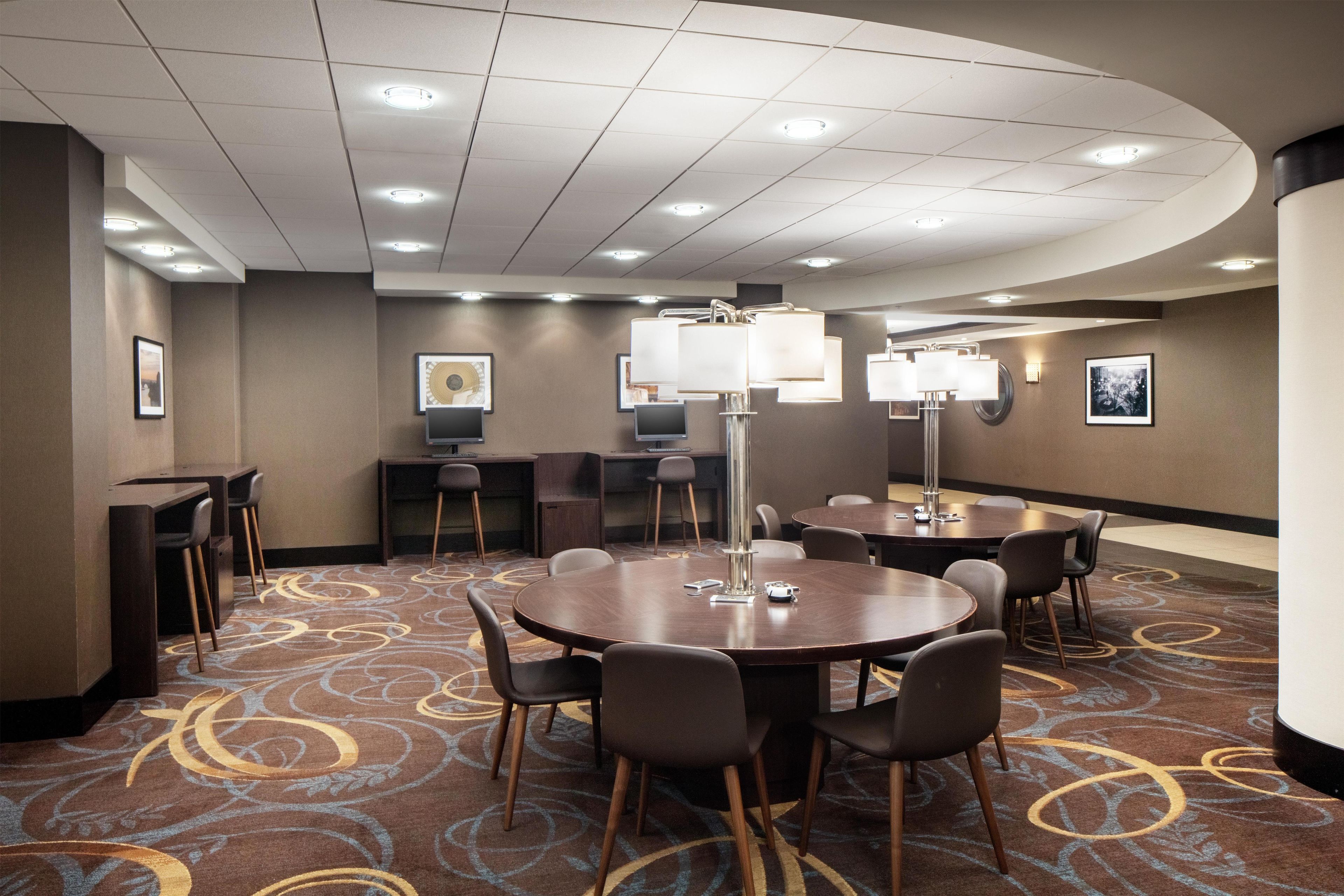 A conference room with a round table, chairs, a large floor lamp, and framed artwork on the walls.