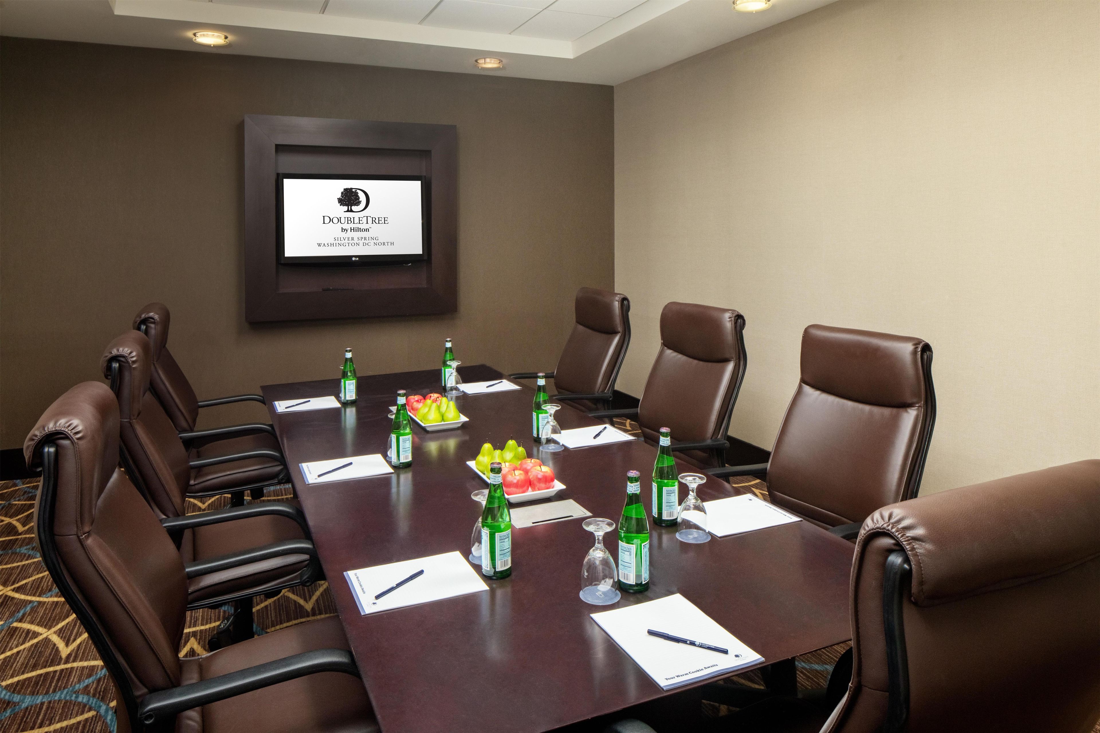 A conference room with a long table, brown leather chairs, and a framed sign on the wall.