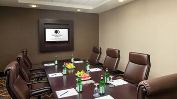 A conference room with a long table, brown leather chairs, and a framed sign on the wall.