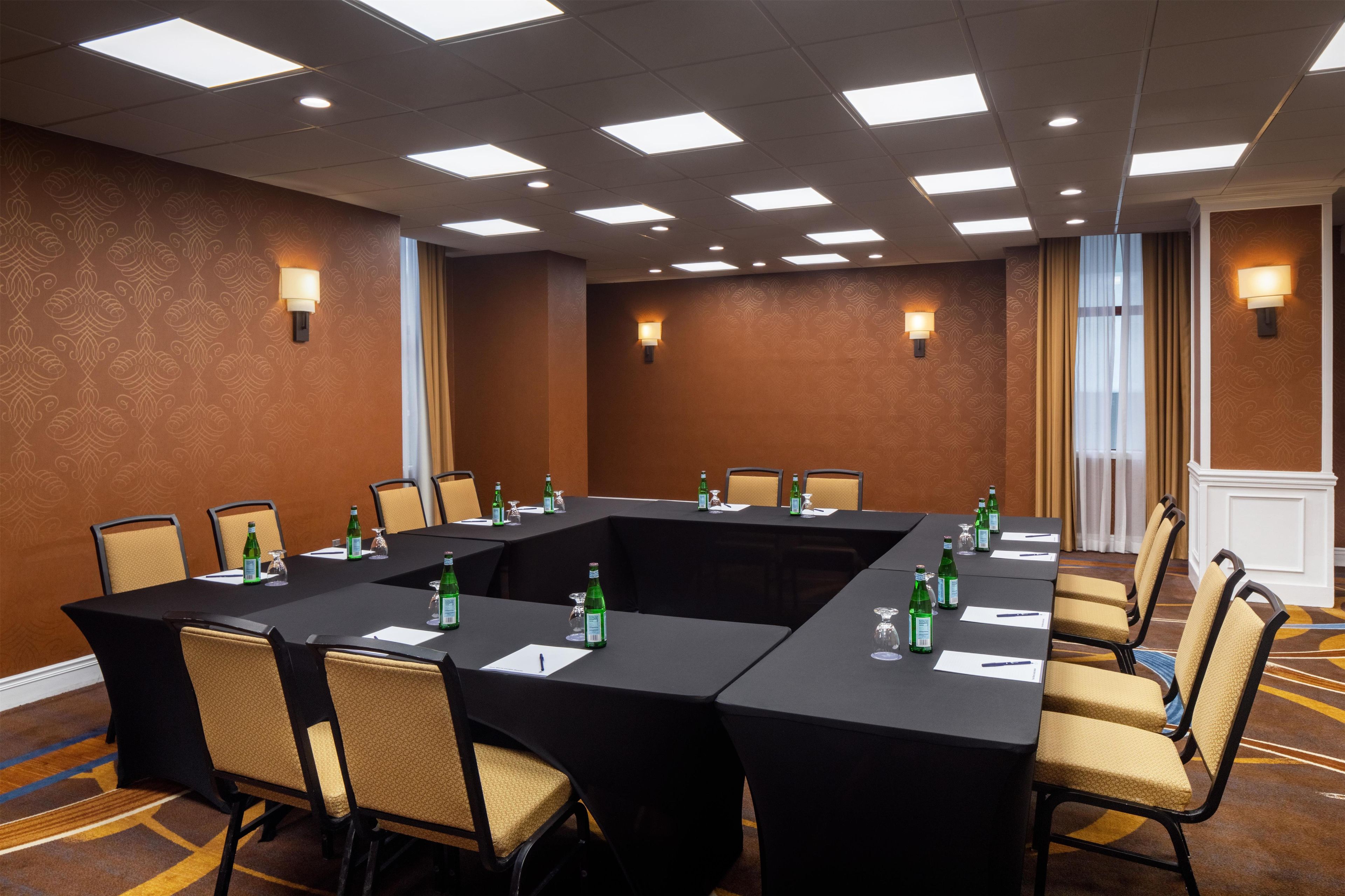 Un salón de conferencias con una mesa rectangular, sillas y lámparas fijadas a la pared.