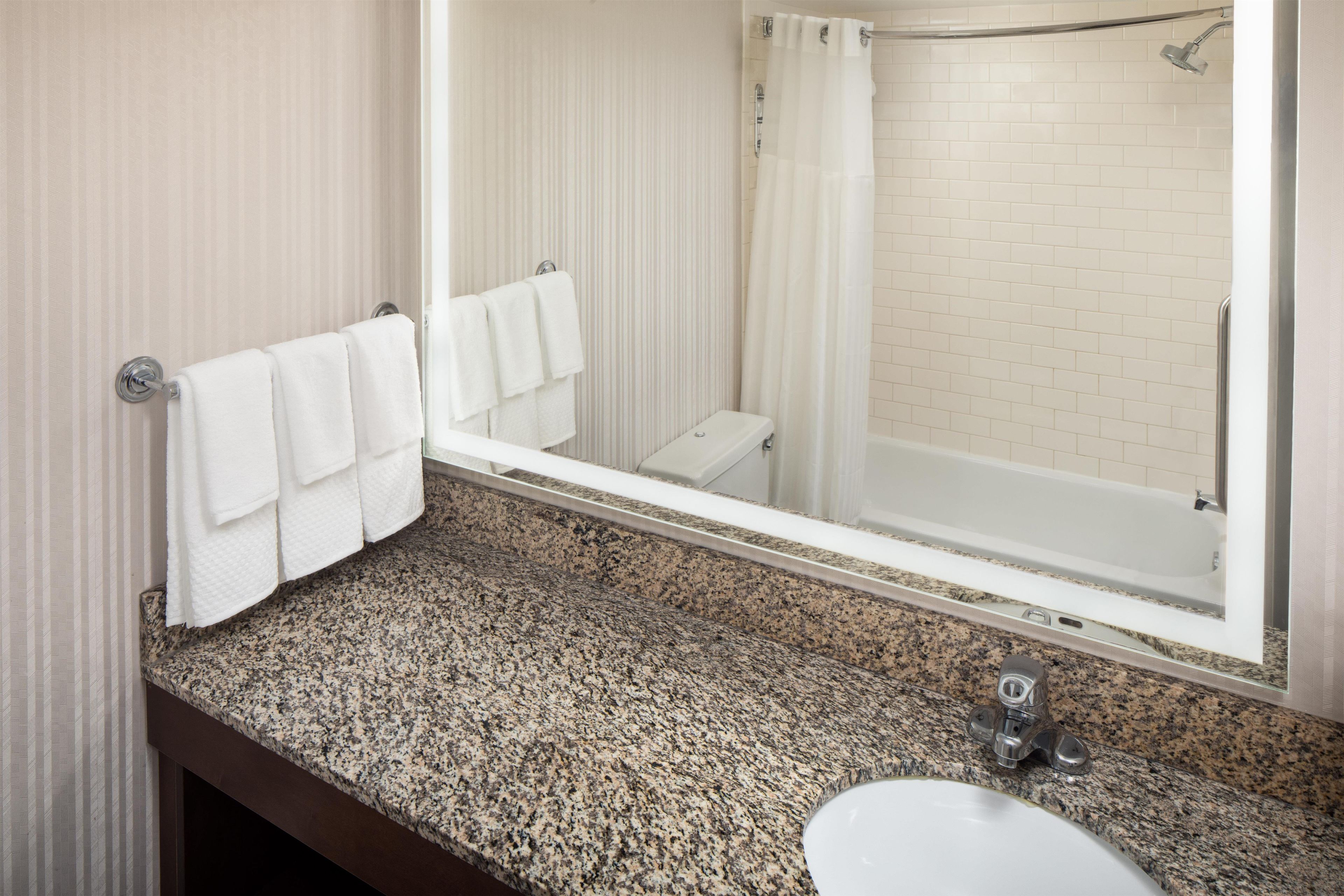 A bathroom with a granite countertop, a sink, a mirror, and a shower area.