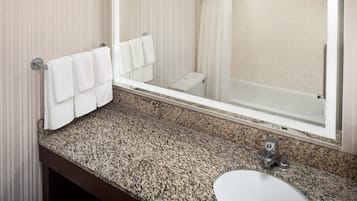 A bathroom with a granite countertop, a sink, a mirror, and a shower area.