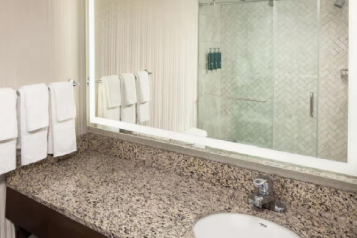 A bathroom with a granite countertop, a sink, and a large mirror reflecting a shower area.