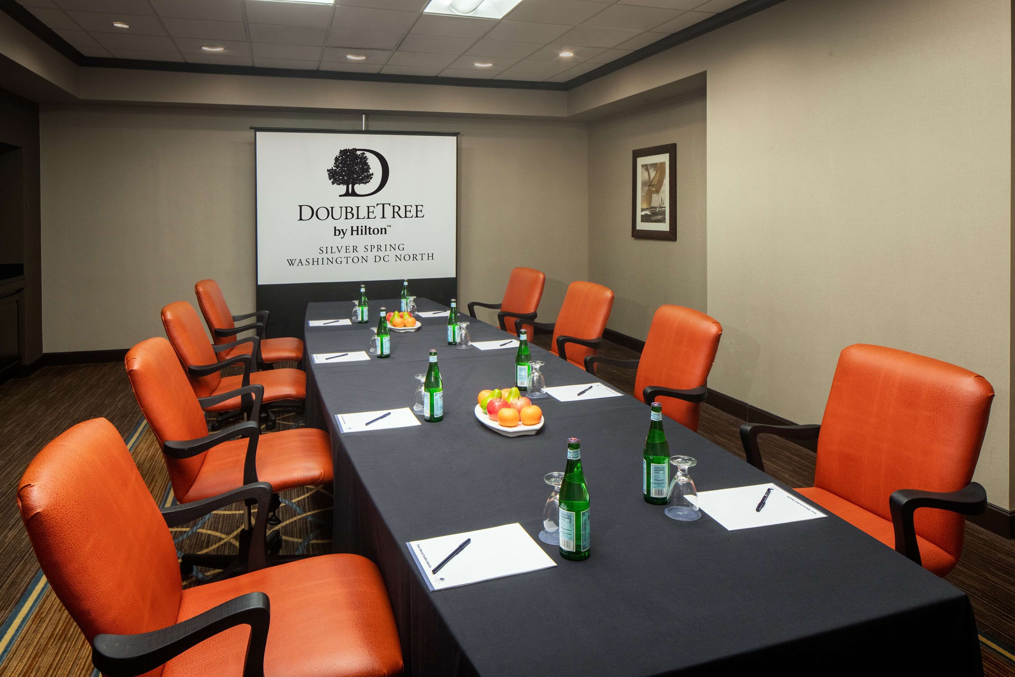 A conference room with a long table, orange chairs, and a projector screen displaying the DoubleTree by Hilton logo.