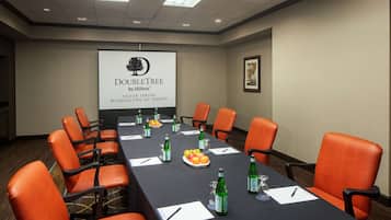 A conference room with a long table, orange chairs, and a projector screen displaying the DoubleTree by Hilton logo.