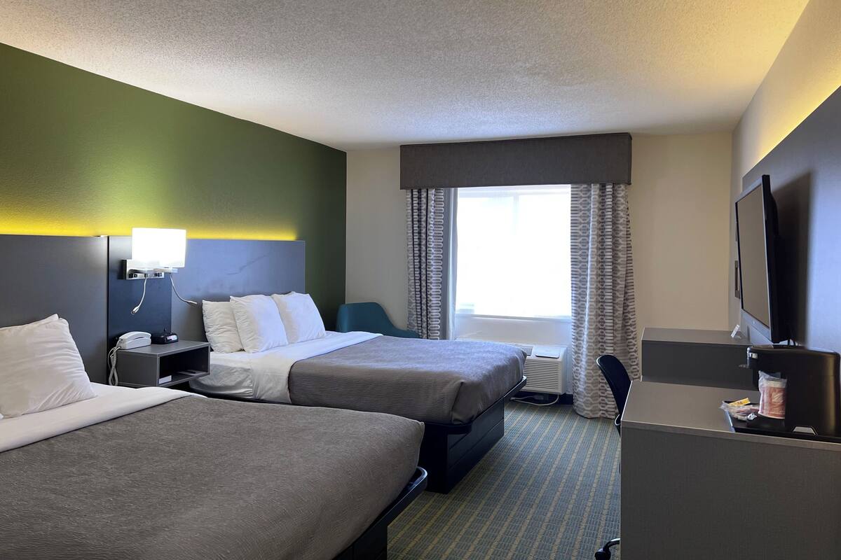 Habitación de hotel con dos camas, un escritorio, televisión, ventana con cortinas y lámpara de pared.