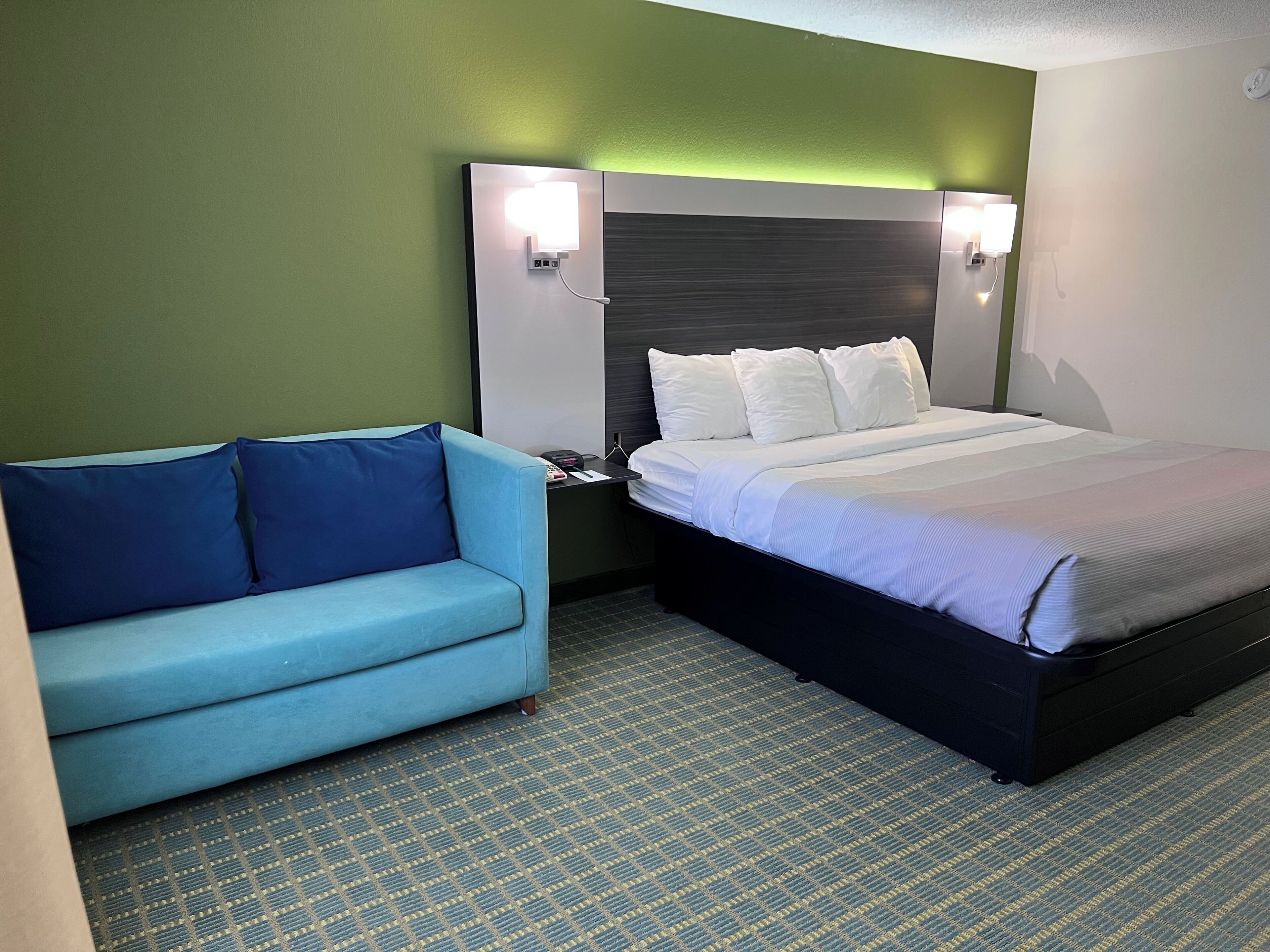 A hotel room with a bed, a blue sofa, and two wall-mounted lights.